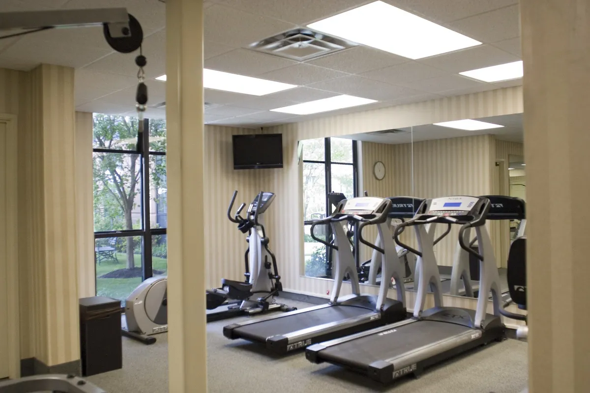 A well-equipped fitness center with treadmills and an elliptical machine facing large windows, letting in plenty of natural light. A wall-mounted television provides entertainment for guests during their workouts, and the clean, modern design encourages a sense of motivation and energy.
