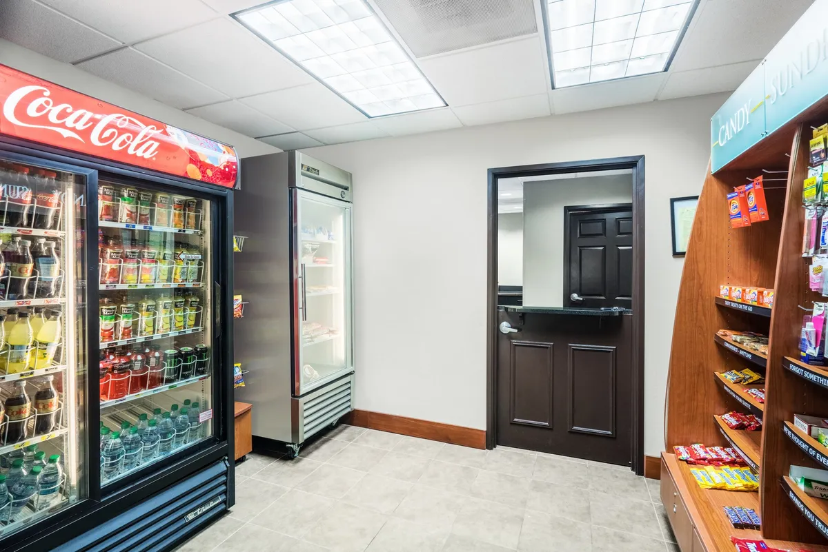 This image features a casual snack area with a Coca-Cola vending machine, a snack display rack, and a refrigerator. The space is designed for quick refreshment, offering guests easy access to drinks and snacks in a relaxed, convenient setting.