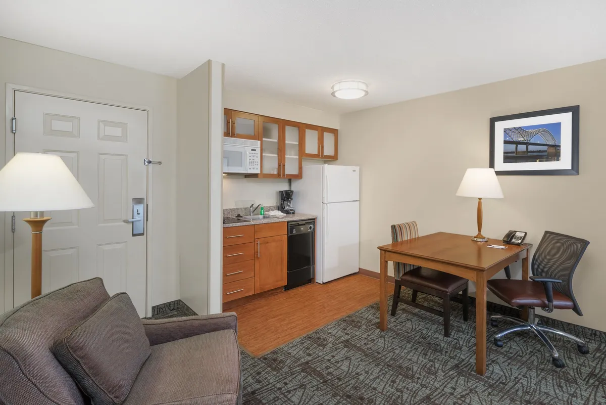 A well-lit, spacious interior featuring an open-plan arrangement that seamlessly incorporates a kitchen area with modern appliances, a dining table for gathering or working, a comfortable sofa ideal for lounging or socializing, and a stylish floor lamp that adds a cozy touch. The layout offers both comfort and versatility, creating an inviting atmosphere for families, friends, or business travelers.