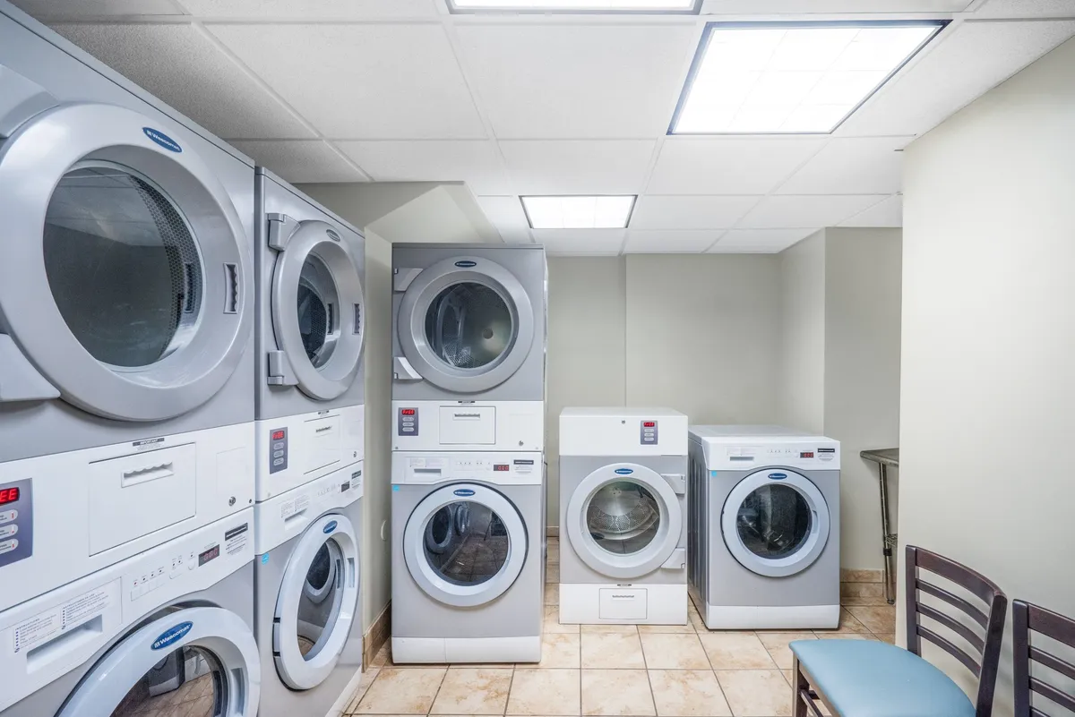 A bright and efficient laundry area featuring multiple stacked washers and dryers, complemented by a comfortable seating area illuminated by overhead lights. The setup conveys convenience and practicality for guests staying longer or traveling with families.